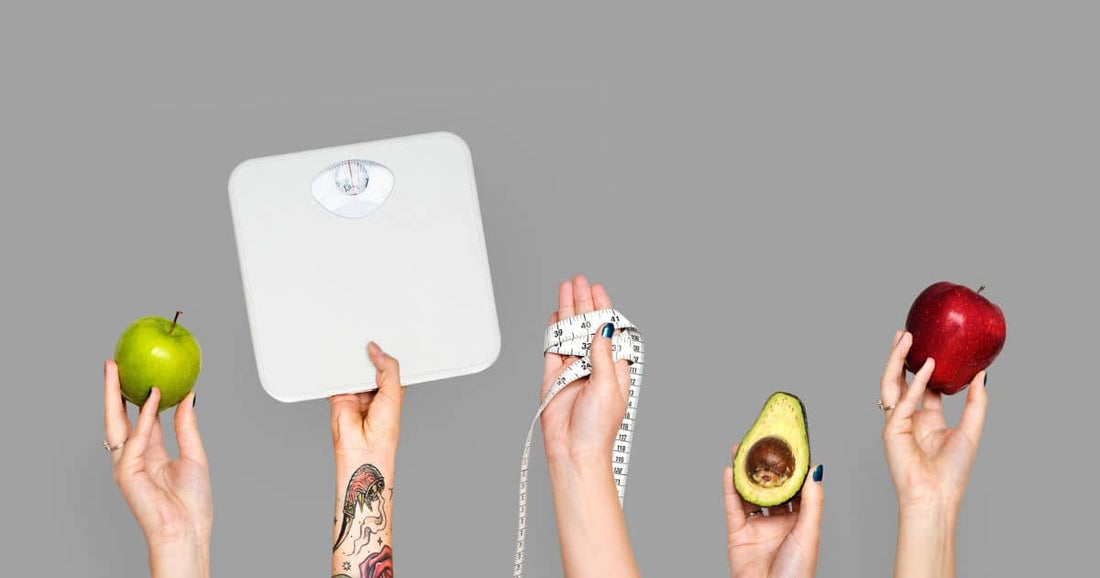 Hände halten Waage, Massband, Obst und Avocado vor grauem Hintergrund.