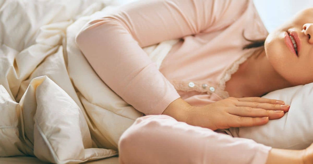 Frau liegt im Bett und schläft in heller Schlafkleidung.