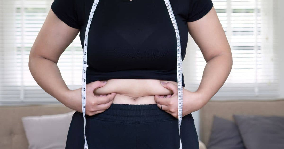 Person kneift in Bauchfett, Maßband hängt über Schultern.